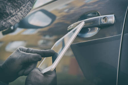 Hooded thief tries to break the car's security systems with tablet. Hacking modern car conceptの写真素材