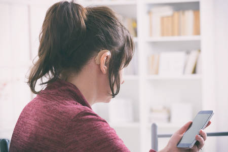 Deaf woman wearing hearing aid and using smartphoneの写真素材