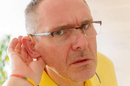 Man wearing deaf aid in ear attempting to hear something
