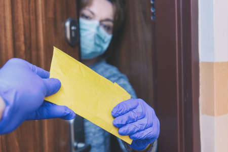 Woman wearing a protective face mask and gloves opening the door and receiving a mail post letter;...