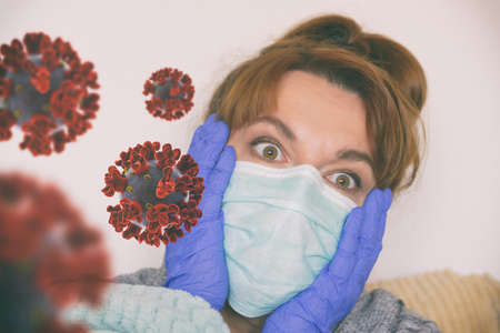 Scared woman sitting at home wearing a protective mask and gloves. Coronavirus pandemic fear conceptの写真素材