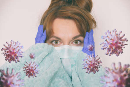 Scared woman sitting at home wearing a protective mask and gloves. Coronavirus pandemic fear conceptの写真素材