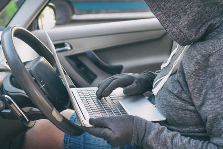 Hooded thief tries to break the car's security systems with laptop. Hacking modern car conceptの写真素材