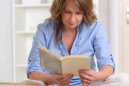 Smiling young woman reading storybook on couch at home