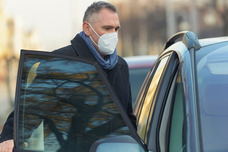 Mature man wearing a face mask during the covid-19 pandemic gets into a car