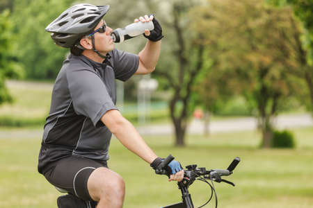 Cyclist drinks water from a bottle while riding a bikeの写真素材