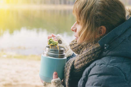 Woman is eating a warm meal from a flask . The concept of eating food outside and having a picnicの写真素材
