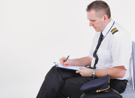Airline captain pilot fills out the paperwork before the flight. A cap and a suitcase are lying next to him.の写真素材