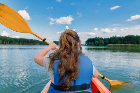 long-haired brunette woman paddles a kayak across a lake, back viewの写真素材