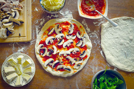 Preparing the Italian pizza known as the Margherita. Yeast dough pizza with mushrooms, mozzarella cheese and tomato sauce.の写真素材