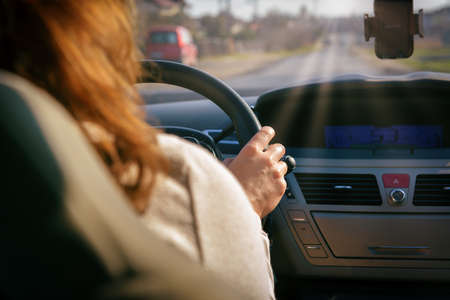 Woman driving a car, close up of her hand at the steering wheel. View from behind
