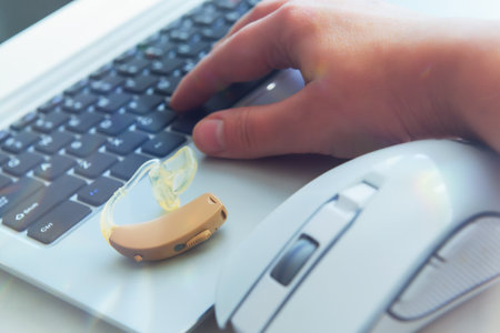 Hearing aid device, woman's hand on laptop keyboard and computer mouse. Work for deaf peopleの写真素材
