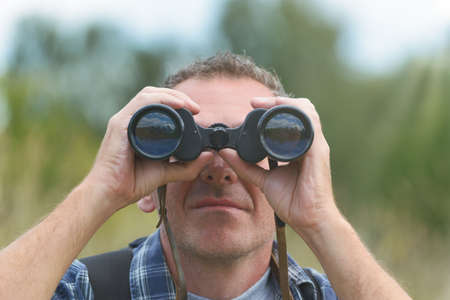 Close up of a man looking through binoculars, outdoors.