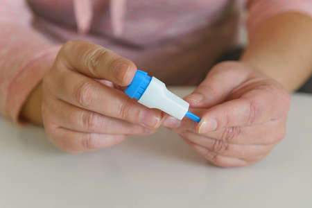 The woman uses a lancing device to take a blood sample from her finger and test for or diabetesの写真素材