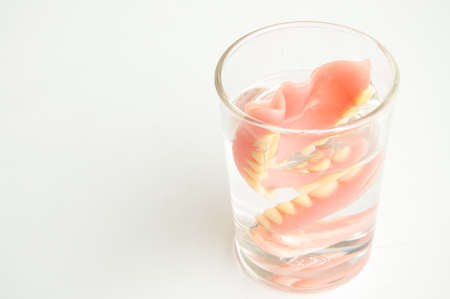 An artificial denture in a glass of water on isolated background