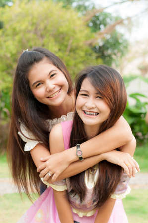 Asian sisters friends embracing and laughing at cameraの写真素材