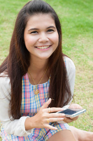 Modern teenager girl using a smart phone in a park with a green の写真素材