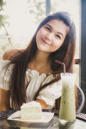 Woman at cafe thinking happy and smiling. Young beautiful Asian female model. Image is cross-processed giving retro style.の写真素材