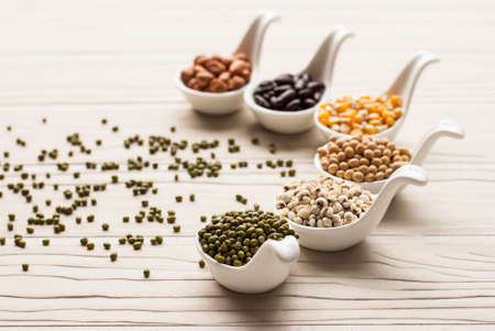collection set of beans, legumes, peas, lentils on ceramic spoons on white wooden backgroundの写真素材