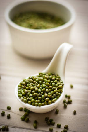Raw mung beans in ceramic spoon over white wooden backgroundの写真素材