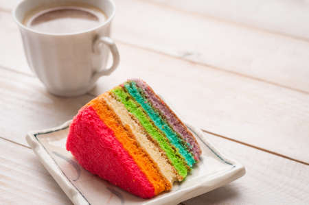 Rainbow cake with white tea cup on the wood tableの写真素材