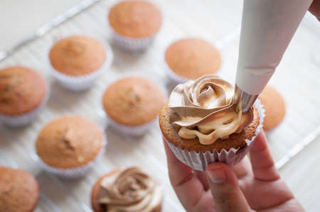 female hands holding piping bag filled with cream cheese and coffee frosting decorating cupcakesの写真素材