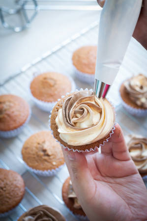 Chef decorating and piping buttercream icing on coffee filled coffee cupcakes - bakeryの写真素材