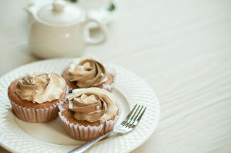 cream cheese and coffee cupcakes with tea pot on white wooden board