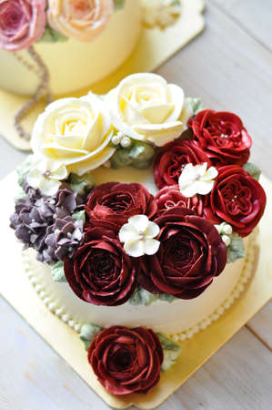 Gorgeous cake covered in roses made of butter cream icing on white wooden background.の写真素材