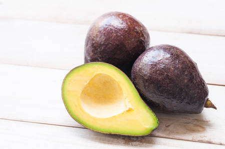 Ripe avocado cut in half on white wooden background