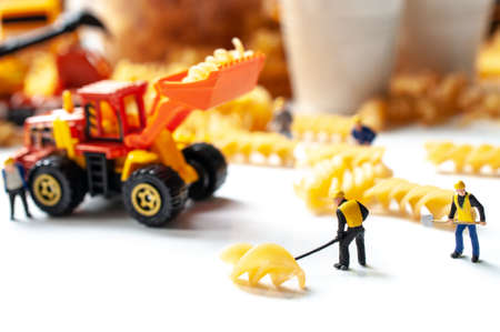 Miniature workers and raw spiral pasta on white backgroundの写真素材