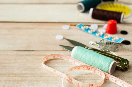 Scissors, measuring tape, buttons and sewing tools on wooden background
