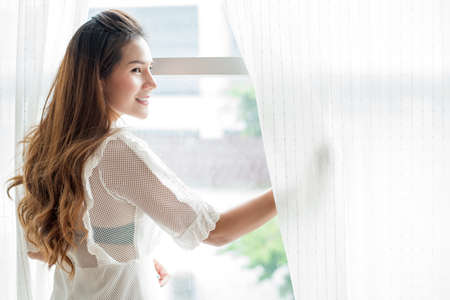 close up of happy woman opening window curtainsの写真素材