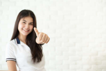 Happy young woman giving thumb up on white brick wall backgroundの写真素材