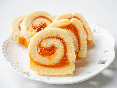 Swiss roll filled with orange jam on white plate