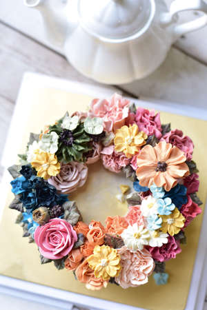 Colorful Buttercream flower cake with teapot on wooden backgroundの写真素材