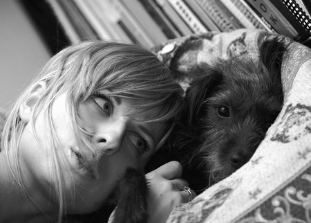 Girl and dog are lying on bed. Black-white photo.