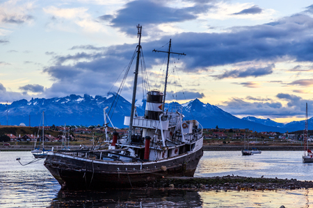 Old broken ship stranded ashore and village with mountains in the background, Ushuaia, Patagonia, Argentinaの写真素材