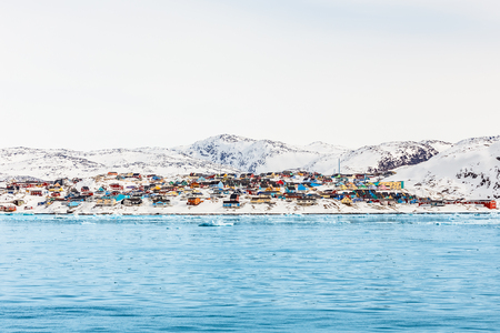 Arctic city panorama with colorful Inuit houses on the rocky hills covered in snow with snow and mountain in the background, Ilulissat, Greenlandの写真素材