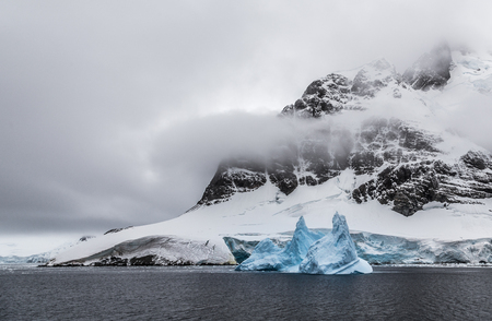 Huge steep stone rock covered with glacier and drifting blue iceberg, close to Argentine islands, Antarcticaの写真素材