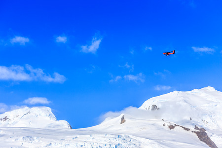 Small red plane flying among clouds over snow peaks and glaciers, Hald Moon island,  Antarctic peninsulaのeditorial素材