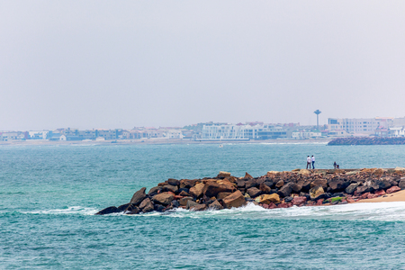 Waves, stones at the coastline with houses in background, Swakopmund German colonial town, Namibiaの写真素材