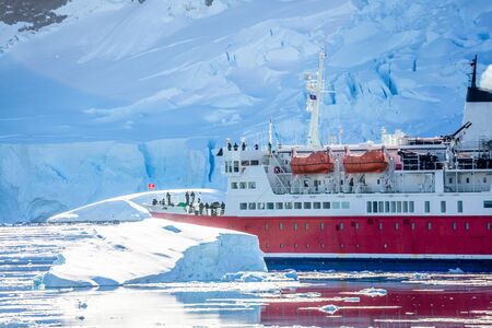 Red cruise passenger liner drifting among the icebergs with glacier sheet in background, Neco bay, Antarcticaの写真素材
