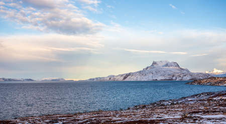 Frozen tundra landscape with cold greenlandic sea and snow Sermitsiaq mountain in the background,...
