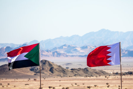 Sudanese and Bahrain flags waving togetner on the wind in Saudi Arabian desertwith mountains in background, Al Ula, Saudi Arabiaの写真素材