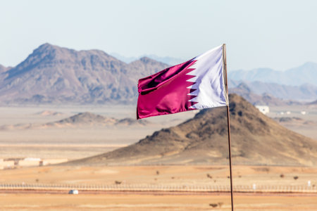 Qatar flag waving on the wind in Saudi Arabian desertwith mountains in background, Al Ula, Saudi Arabiaの写真素材
