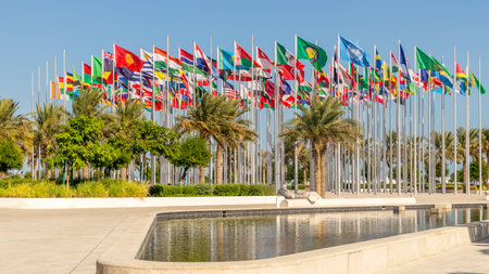 Many worlds countries national flags waving on the wind, with UN, EU, GCC banners with palms and pond in the foreground, Doha, Qatarの写真素材