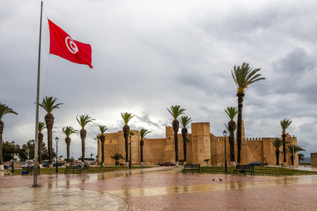 Tunisian national flag with lots of palms and Ribat of Monastir under cloudy skies, Monastir, Monastir Governorate, Tunisiaの写真素材