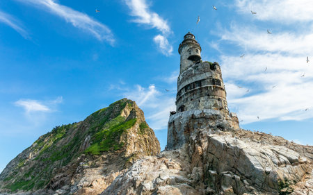 Close upward view of abandoned Japanese Aniva Lighthouse on Sakhalin, Russia with rusted concrete walls and seabirds on rocky foregroundの写真素材
