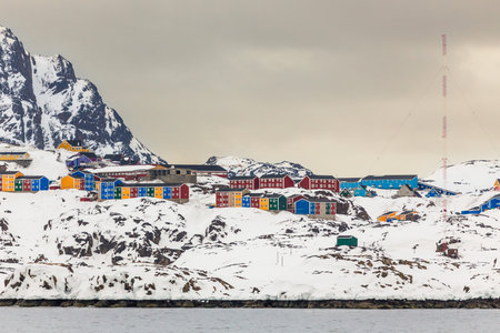 Wide coastal panorama of Sisimiut with colorful Inuit houses, snow covered terrain and steep arctic...